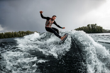 Male wakesurfer having fun rides wave on surfboard in the summer day