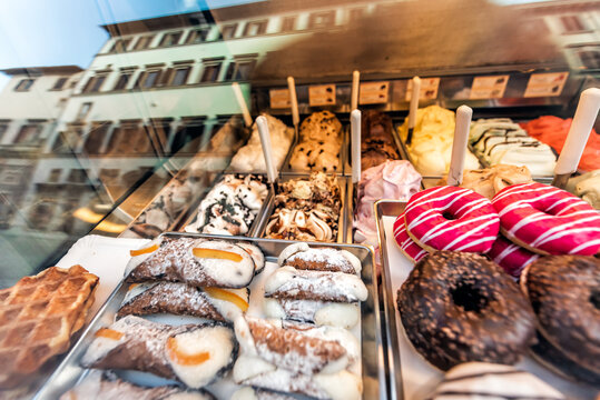 Assortment variety of many chocolate pink sugar icing donuts with traditional cannoli dessert on window display in bakery in Italy