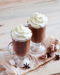 Two glasses of cocoa with whipped cream on a light wooden background. Selective focus.