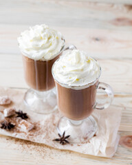Two glasses of cocoa with whipped cream on a light wooden background. Selective focus.
