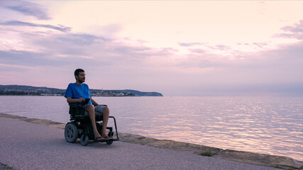 Man on wheelchair near sea at sunset.