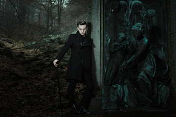 Aristocratic vampire leaning to graveyard statue - obrazy, fototapety, plakaty