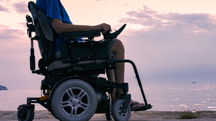 Man on wheelchair near sea at sunset.