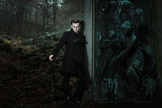 Aristocratic vampire leaning to graveyard statue