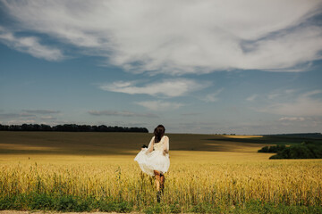 Girl enjoying nature. Beautiful girl in white dress walking on the field.