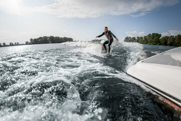 view on guy who rides surfboard on the waves behind boat.