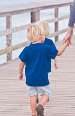 back view, close distance, of twin boys, holding mothers hand, while waling on wood pier, into tropical waters, of gulf of Mexico, on a sunny day