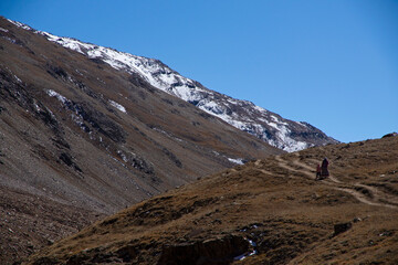 Two persons - tourists - a mother and a child walk on a narrow route on a hill near Chandratal on a clear day with blue sky.