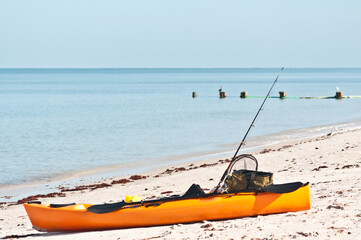 side view, medium distance of a yellow kayak, set up for fishing, resting on a sandy beach at the shoreline of a tropical beach, on gulf of Mexico on sunny day