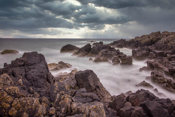 Fototapeta na wymiar Rocky scottish coastline on a stormy day. Dark clouds and dark rocks looking out to sea