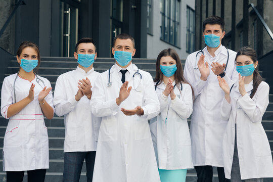 Medical staff from the hospital who are fighting coronavirus applaud back the people and police officers for their support. Group of doctors with face masks. Corona Virus and Healthcare Concept