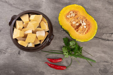 Top view of kabocha pieces on a bowl with half fruit, pepper and herbs
