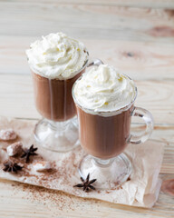 Two glasses of cocoa with whipped cream on a light wooden background. Selective focus.