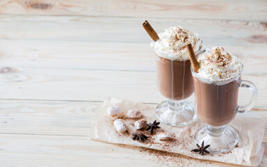Two glasses of cocoa with whipped cream on a light wooden background. Selective focus. Copyspace