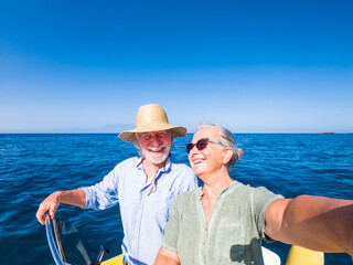 couple of cute mature people or senior ejoying and having fun together in the middle of the sea or ocean with a small boat or dighy - woman pensioner taking a selfie with her old man driving the boat