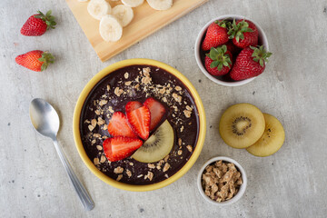 Brazilian typical acai bowl with fruits and muesli over wooden background. Top view