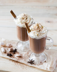 Two glasses of cocoa with whipped cream on a light wooden background. Selective focus.