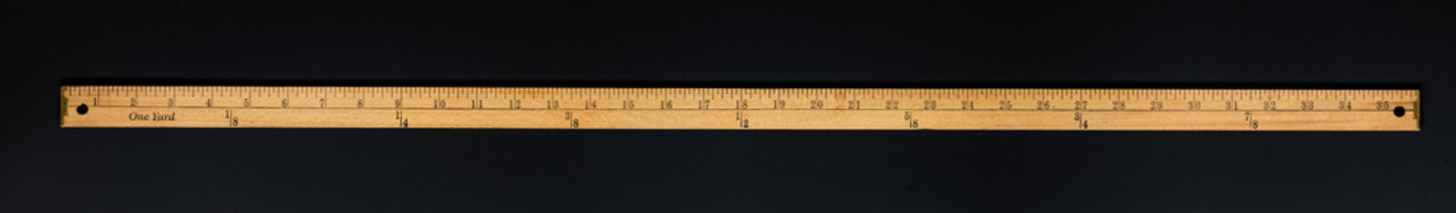 Wooden yardstick on black backgrounds whit inches and yard fractions scales.