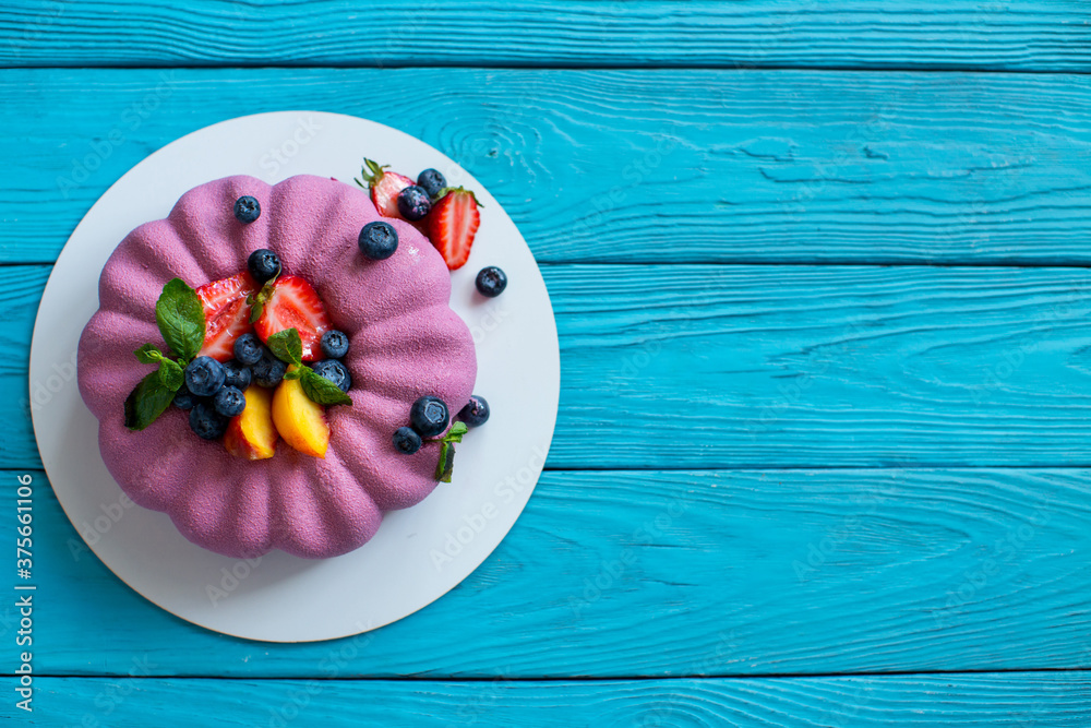 Poster Pink cake garnished with slices of peach, strawberries, blueberries and mint leaves on a wooden blue background. Vegan dessert