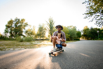Smiling man together with his little daughter riding skateboard on the road in summer park © fesenko