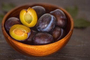 ripe plums in a wooden bowl close-up. background with whole plums and half plums.