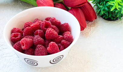 Raspberries in a white bowl on a light background with tulips.