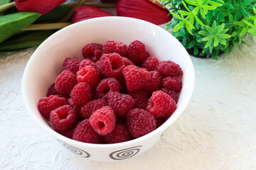 Raspberries in a white bowl on a light background with tulips.