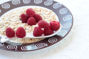Dry oatmeal with raspberries on a white background with a ceramic spoon.