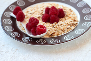 Dry oatmeal with raspberries on a white background with a ceramic spoon.