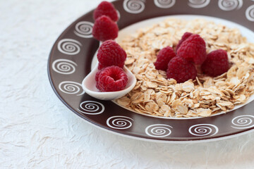 Dry oatmeal with raspberries on a white background with a ceramic spoon.