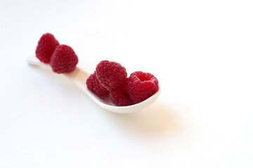 Ripe raspberries in a ceramic spoon on a white background.