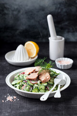 Fresh vegetables salad (radishes, cucumbers, avocado, celery, dill, green onions) with yogurt dressing and canned cod liver, selective focus