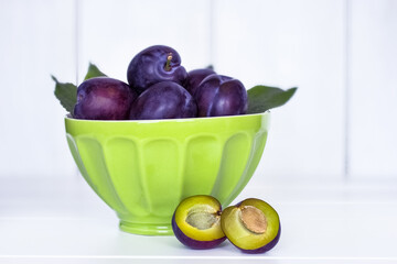 ripe plums in a green ceramic bowl close-up. background with plums in a bowl on a white background. plums on the table close-up.