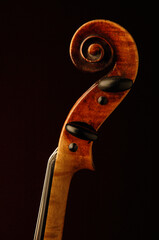 Antique well used violin scroll with ebony pegs sideview on black background