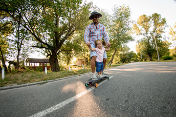young man with little child practicing skateboarding in park.