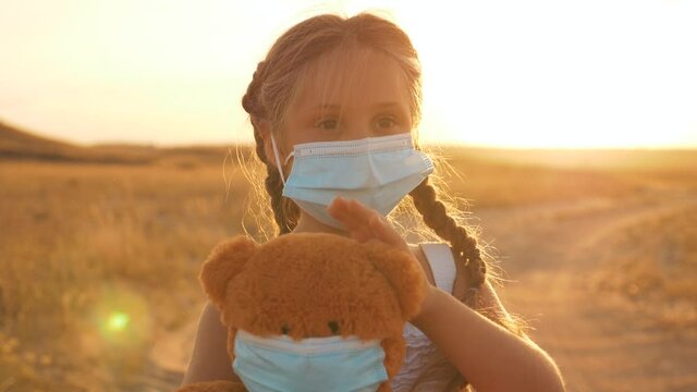 A child stands on the field with a soft toy in his hands. A child in a medical mask isolated during the quarantine of the virus. A kid plays doctor with a Teddy bear. The concept of health care.