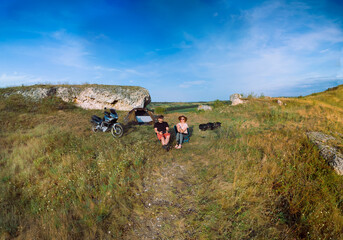 A man and a woman enjoy the view from the top of the mountain, sunset. Front view, extreme tourism in the wild. Travel equipment. Camping tent and touring motorcycle. Bikers vacation.