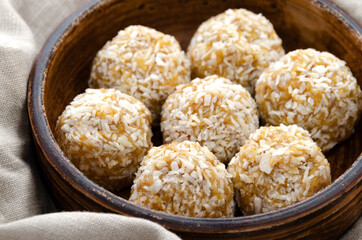 Raw vegan healthy sweets, energy balls with dried fruits and coconut. Brown plate with a napkin. Top view