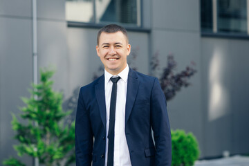 Handsome smiling confident businessman portrait. Modern businessman. Confident young man in suit looking away while standing outdoors with cityscape in the background
