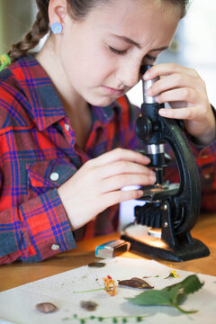Young girl looking at various things through an old school microscope in her home