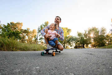 Happy man with girl are sitting on skateboard in the park road. © fesenko