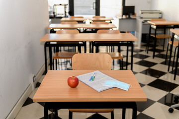 Desk with an apple, medical mask and a copybook in an empty classroom, new normal, back to school during Covid-19