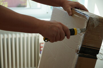 Obraz premium A man opening a cardboard parcel with furniture parts for DIY assembly. Close up photo with detail on the working process for improving his home.