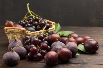Obraz premium Still life of fruits. Bunch of grapes in wicker basket. Figs and plums on table
