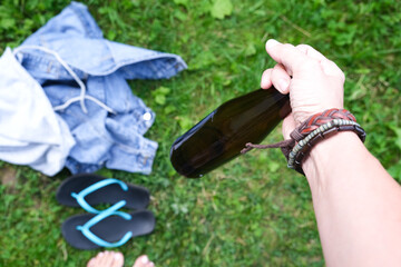 A hand of a hippie, hipster holding a bottle of alcohol, beer. Young people with alcohol addiction concept. Summertime joy and picnic