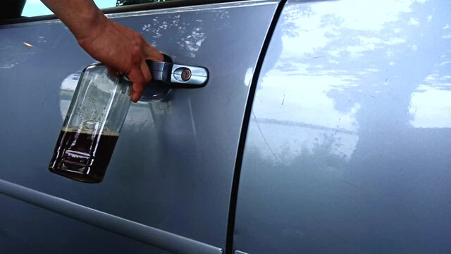 Soft focus video. Drunk driver is opening the car door. Man is holding a bottle and keys. Alcohol while driving. Accident from addiction problem