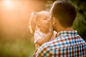 Rear view of man holding his daughter in his arms on sunny summer day.