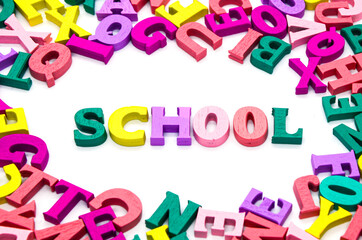 Word "school" is laid out of wooden multicolored letters surrounded by scattered colored letters on white background. Concept: back to school, literacy and reading, language learning