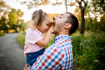 little girl sits in her father's arms and carefully looks into his mouth