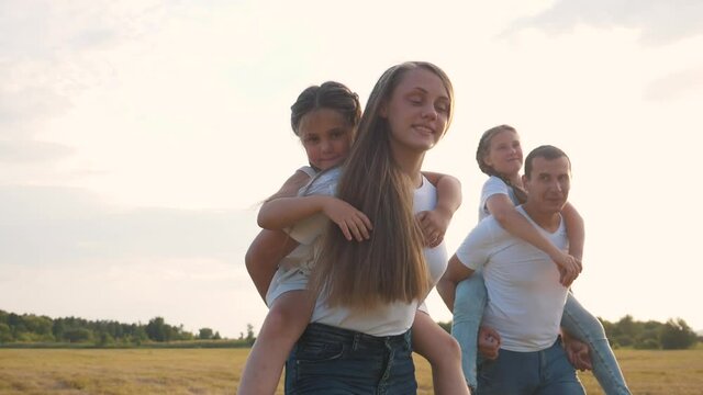 Happy family, children have fun with their parents. Dad and mother play with children, carry daughters on their backs. Cheerful family in the park.